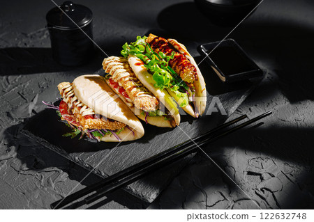 Delicious Asian-inspired bao buns filled with crispy chicken, vegetables, and sauces on a slate platter 122632748