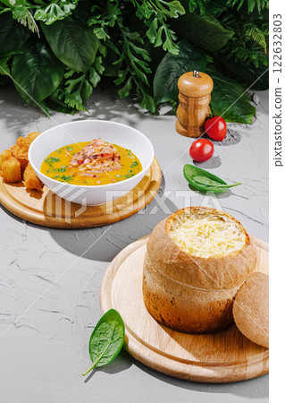 Delicious soup and bread bowl served on a wooden platter with vibrant greens 122632803