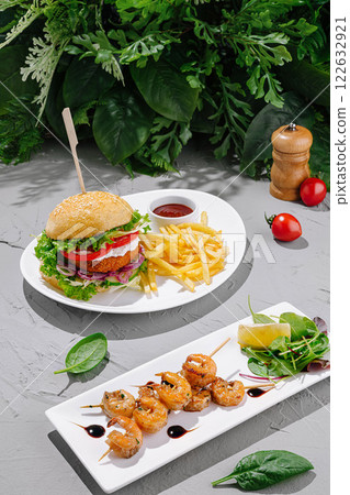Delicious burger and shrimp skewer meal served with fries and garnished with fresh ingredients in a vibrant setting 122632921