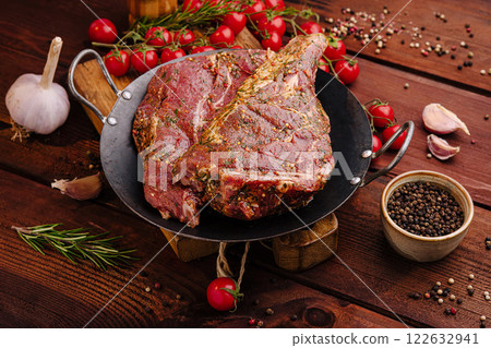 Marinated beef steaks prepared for grilling with fresh herbs and vegetables on a rustic wooden table 122632941