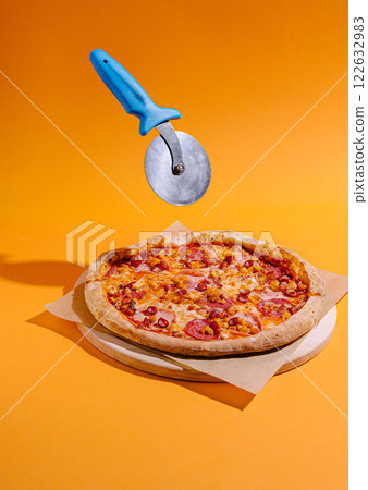 Pizza with vibrant orange background and a pizza cutter floating above ready for slicing Pizza with vibrant orange background and a pizza cutter floating above ready for slicing 122632983