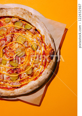 Unique pizza featuring pickles and spiral sauce served on a wooden platter against a bright orange background 122632987