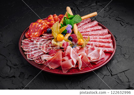 Cured meats and fruits arranged beautifully on a dark platter for a gourmet presentation Cured meats and fruits arranged beautifully on a dark platter for a gourmet presentation 122632996