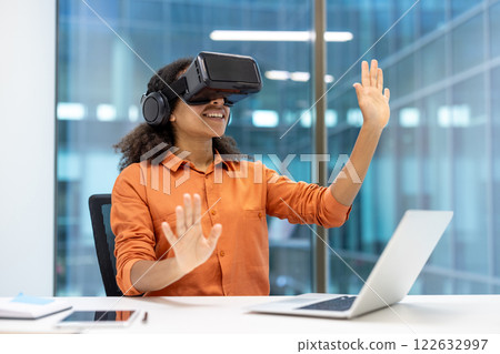 Woman using VR headset at desk, immersed in virtual environment. Professional setting highlights technology's role in innovation, creativity, and productivity in office work. Woman using VR headset at desk, immersed in virtual environment. Professional setting highlights technology's role in innovation, creativity, and productivity in office work. 122632997