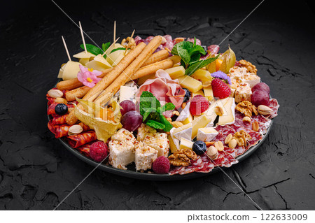 Exquisite charcuterie platter featuring a variety of cheeses, meats, fruits, and nuts displayed elegantly for a festive gathering Exquisite charcuterie platter featuring a variety of cheeses, meats, fruits, and nuts displayed elegantly for a festive gathering 122633009