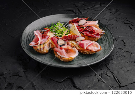 Delicious charcuterie platter featuring assorted meats and cheeses served elegantly on a black plate Delicious charcuterie platter featuring assorted meats and cheeses served elegantly on a black plate 122633010