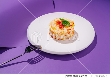 Colorful rice dish garnished with herbs on a modern plate against a vibrant purple background 122633025