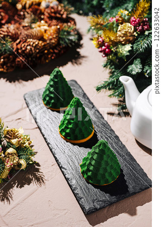 Holiday dessert display featuring festive green conical pastries with a teapot on a rustic table setting 122633042