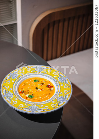 Delicious bowl of vibrant soup served in an artistic plate on a sleek table in a modern dining room setting Delicious bowl of vibrant soup served in an artistic plate on a sleek table in a modern dining room setting 122633067