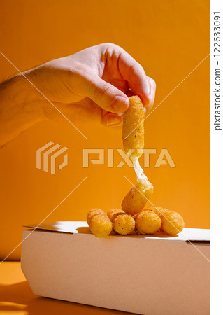 Delicious mozzarella sticks being lifted from a white takeout box against a vibrant orange background 122633091