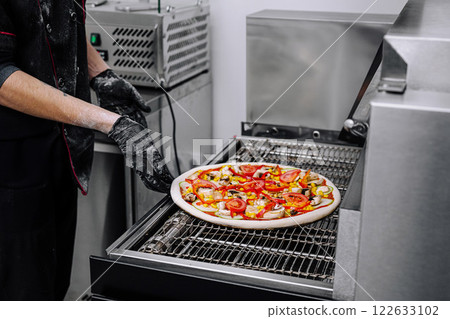 Chef preparing pizza with fresh vegetables on grill in modern kitchen environment Chef preparing pizza with fresh vegetables on grill in modern kitchen environment 122633102