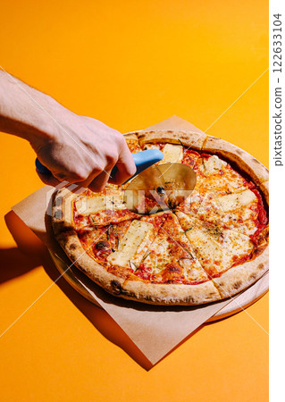 Delicious pizza being cut with a circular cutter on a vibrant yellow background 122633104