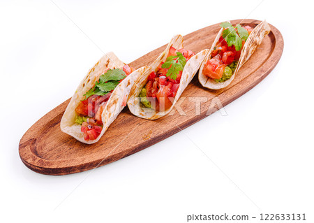 Three colorful tacos on a wooden platter with fresh toppings ready to serve at a casual dining setting 122633131