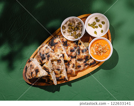 Delicious freshly baked flatbread served with assorted dips on a wooden platter against a green background 122633141