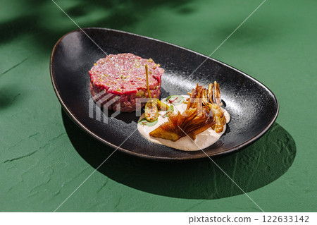 Delicious tartare with unique garnishes served on an elegant plate against a vibrant green background Delicious tartare with unique garnishes served on an elegant plate against a vibrant green background 122633142