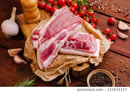 Fresh pork ribs with tomatoes, garlic, and herbs arranged on a wooden table for a home cooking preparation Fresh pork ribs with tomatoes, garlic, and herbs arranged on a wooden table for a home cooking preparation 122633157