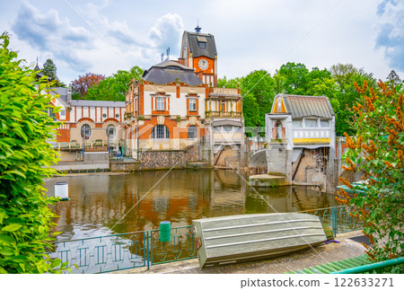 The Art Nouveau Hucak hydroelectric power station stands elegantly along the river in Hradec Kralove, Czechia, surrounded by lush greenery and showcasing its unique architectural design. The Art Nouveau Hucak hydroelectric power station stands elegantly along the river in Hradec Kralove, Czechia, surrounded by lush greenery and showcasing its unique architectural design. 122633271