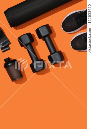 Fitness background with black exercise equipment, dumbbells, mat, elastic band, fitness band, sneakers on orange background. Fitness, sports items, healthy lifestyle. Place for your text Fitness background with black exercise equipment, dumbbells, mat, elastic band, fitness band, sneakers on orange background. Fitness, sports items, healthy lifestyle. Place for your text 122633420