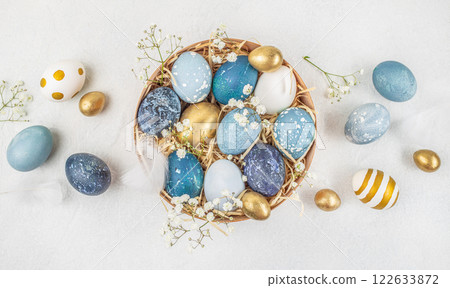 Basket with painted Easter eggs on white background surrounded by flowers. Stylish golden and blue eggs. top view Basket with painted Easter eggs on white background surrounded by flowers. Stylish golden and blue eggs. top view 122633872