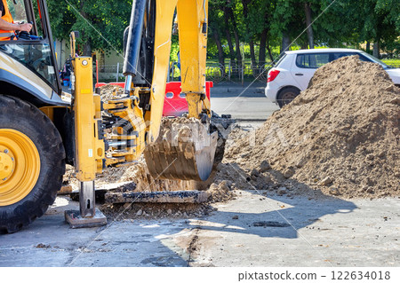 Excavator digging up asphalt on a sunny day in a busy urban street 122634018