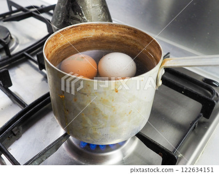 Chicken eggs are boiled in a dirty aluminum pan on a gas stove 122634151
