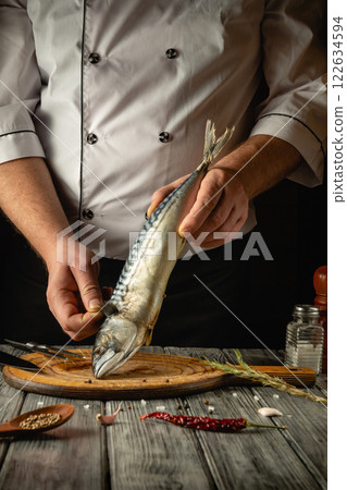 Chef cooks mackerel or scomber in the kitchen. Concept of cooking fish food for restaurant or hotel. Cozy atmosphere on the kitchen table with spices and herbs Chef cooks mackerel or scomber in the kitchen. Concept of cooking fish food for restaurant or hotel. Cozy atmosphere on the kitchen table with spices and herbs 122634594