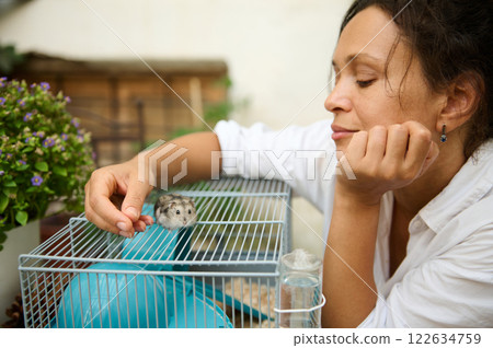 Woman interacting with a cute hamster in a cage outdoors 122634759