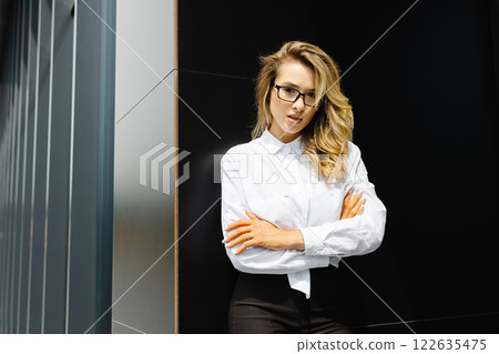 Businesswoman is standing at the corporate building. Confident caucasian woman in glasses is looking to the camera Businesswoman is standing at the corporate building. Confident caucasian woman in glasses is looking to the camera 122635475