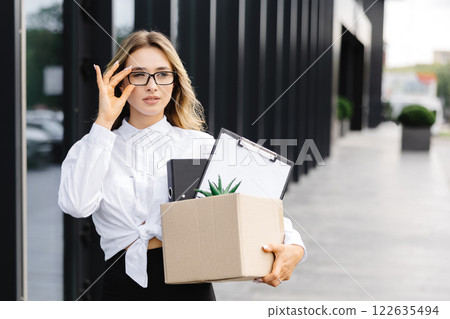 Caucasian businesswoman walking outdoors with box of stuff leaving business. Female office worker lost her job. Fired woman coming back home Caucasian businesswoman walking outdoors with box of stuff leaving business. Female office worker lost her job. Fired woman coming back home 122635494