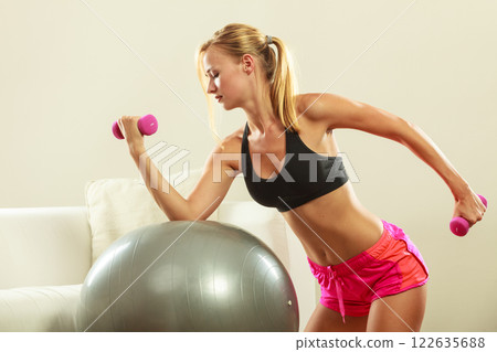 Woman with gym ball and dumbbell doing exercise 122635688