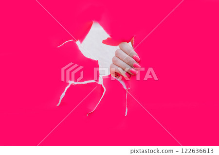 female hand with beautiful nails with pink manicure in pink paper hole 122636613