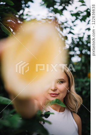 Outdoor portrait of beautiful young woman holding halved lemon fruits 122636638
