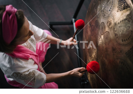 Middle aged woman hitting big gong with soft hammers in yoga studio. 122636688