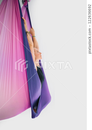 Fit smiling woman in black workout suit practicing fly yoga stretching in hammock 122636692