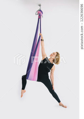 Fit smiling woman in black workout suit practicing fly yoga stretching in hammock 122636696