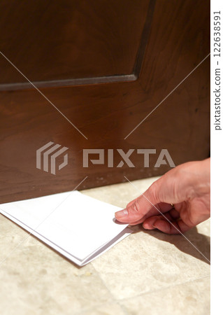 A man carefully slides a sheet of paper under the door 122638591