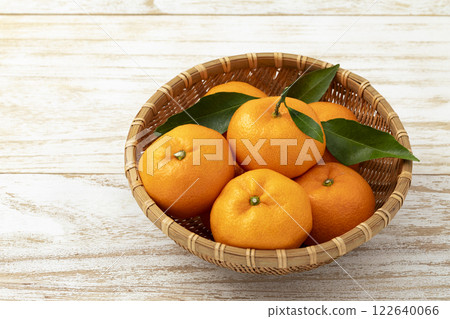 Mandarins with leaves placed in a deep colander on a plain wooden surface Mandarins with leaves placed in a deep colander on a plain wooden surface 122640066