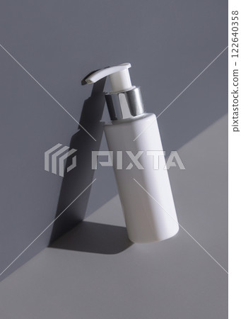 Blank cream bottle on two tones grey background with hard shadow closeup, cosmetic mockup 122640358