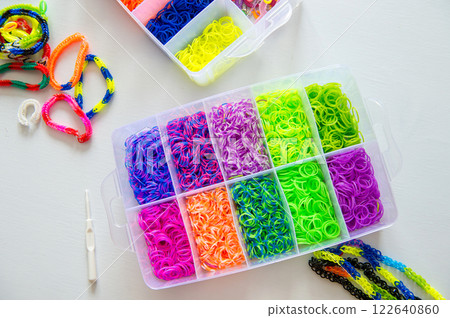 Box of colorful loom bands and bracelets on white table. 122640860