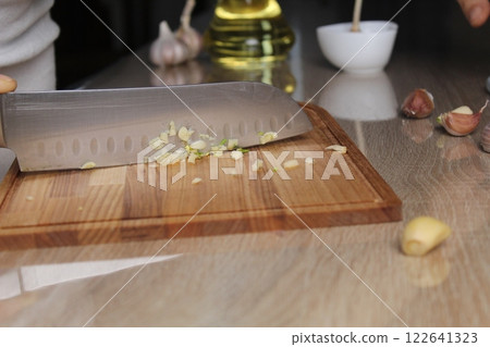 A knife and fine garlic on a cutting board, butter in the background. Garlic Slicing Methods A knife and fine garlic on a cutting board, butter in the background. Garlic Slicing Methods 122641323