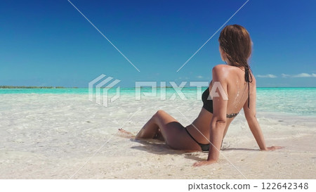 Young woman is enjoying the sun and the turquoise water of a tropical beach in the maldives. She is sitting in the shallow water, taking in the beauty of the ocean and the islands Young woman is enjoying the sun and the turquoise water of a tropical beach in the maldives. She is sitting in the shallow water, taking in the beauty of the ocean and the islands 122642348