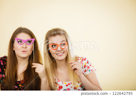 Two happy women holding fake eyeglasses on stick 122642795
