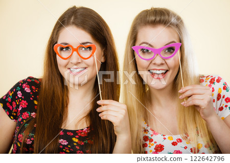 Two happy women holding fake eyeglasses on stick 122642796