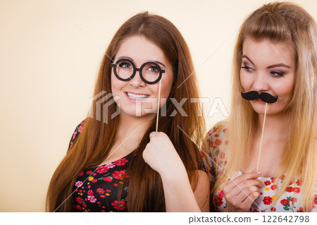 Two women holding moustache and eyeglasses on stick Two women holding moustache and eyeglasses on stick 122642798