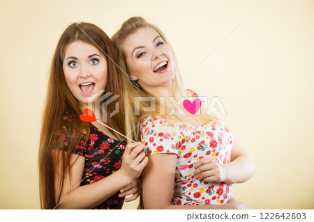 Two happy women holding heart on stick Two happy women holding heart on stick 122642803