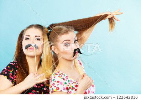 Two happy women holding fake moustache on stick 122642810