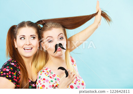 Two happy women holding fake moustache on stick 122642811