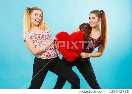 Happy two women holding heart shaped pillow 122642818