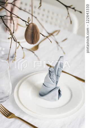 Easter table setting with bunny ear napkins and paper eggs hanging on branches. 122643330
