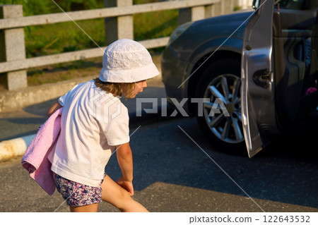 Little girl in a panama hat with a bathing towel walking to a car 122643532